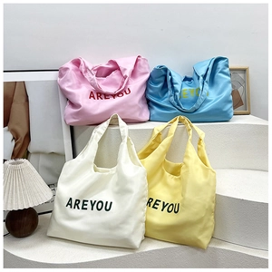 Gros plan de quatre sacs cabas colorés en satin avec lettrage ARE YOU dans une boutique