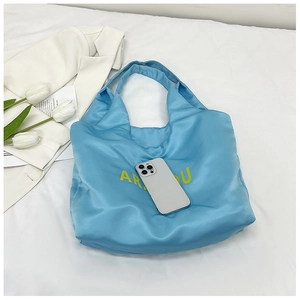 Détail du cabas matelassé bleu clair avec texte jaune et un smartphone blanc