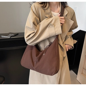 Gros plan du sac hobo marron à surpiqûres contrastées porté sur un trench-coat kaki élégant