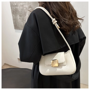 Close-up of a white leather underarm bag with a gold buckle worn with a black coat