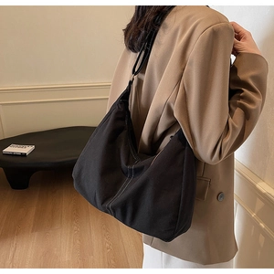 Détail du sac hobo en toile noire avec surpiqûres blanches contrastées porté par un modèle