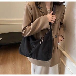 Détail du sac cabas en toile noire avec lanières en cuir marron et coutures blanches