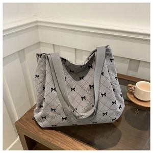 Dettaglio della borsa tote in velluto grigio con fiocco nero e motivo a rombi su tavolo