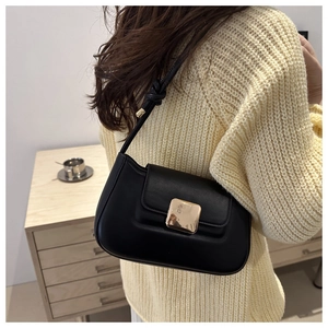 Close-up of black leather baguette bag with gold buckle on shoulder of model