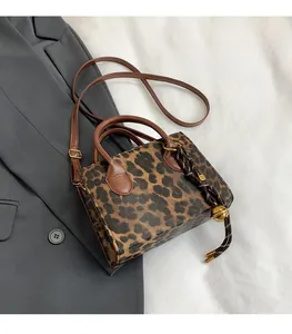Detail of leopard print crossbody bag with leather handles and gold bell charm on grey blazer