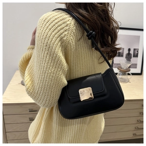Detail of black leather underarm bag with gold metal buckle on a cozy beige sweater