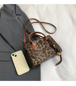 Detailed leopard print handbag featuring a gold bell charm and brown leather handles