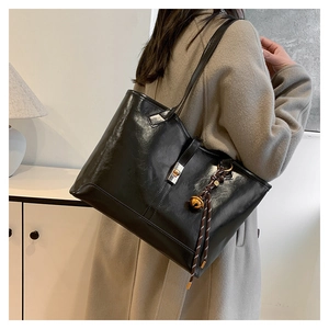 Detail of a black large-capacity tote bag with silver metal lock and braided pendant