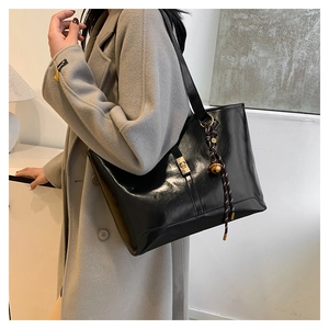 Detail of black faux leather tote bag with metal twist lock and bell charm accessory