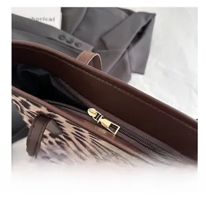 Detailed close-up of the smooth gold metal zipper and brown leather trim on leopard tote