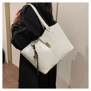 Close-up of a white glossy tote bag featuring a gold buckle and woven charm with bell