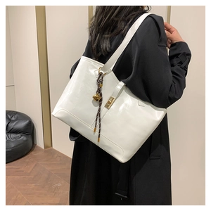 Detailed view of a white tote bag featuring a metal clasp and elegant bell charm on model