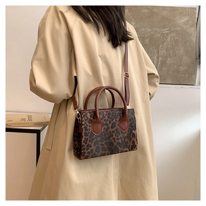 Detail of leopard print handbag with leather handles and gold metal hardware on beige coat