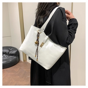 Detailed close-up of a white tote bag featuring a gold twist-lock and a woven bell charm