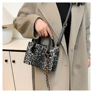 Detail of grey leopard print handbag with black leather handle and woven rope charm
