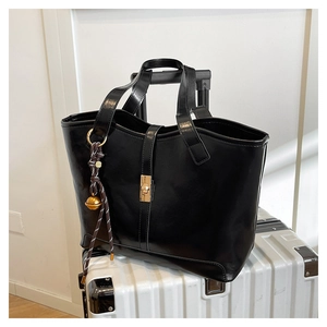 Detail of black faux leather tote with golden twist lock on white luggage case