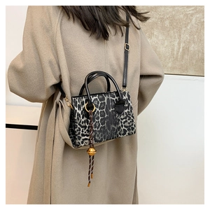 Detail view of leopard print crossbody bag with golden bell charm on wool coat