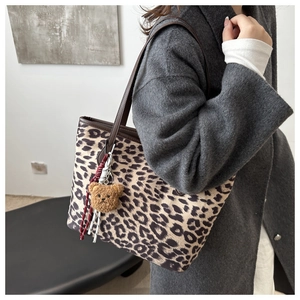 Detail of leopard print tote bag featuring brown leather straps and a plush bear charm
