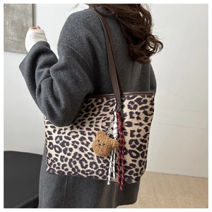 Detail of leopard print tote bag with brown leather strap and plush bear pendant accessory
