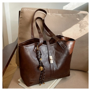 Close-up of vintage brown tote bag with metal lock and a decorative woven bell pendant
