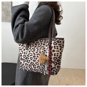 Close-up of leopard print tote bag with brown leather straps and plush bear charm decoration