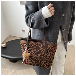 Leopard print tote bag with brown straps and cute plush bear charm on a model's arm