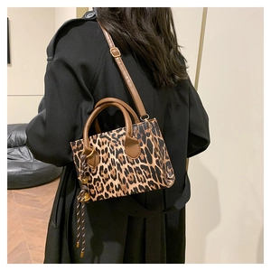 Detail of fashion leopard print crossbody bag with brown leather handles and woven strap