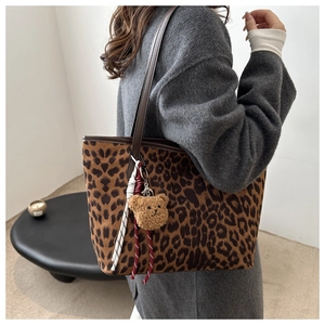 Detail of leopard print tote bag with plush bear charm and woven cord on grey sweater