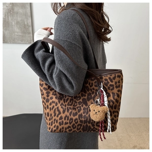 Close-up of leopard print tote bag with brown straps and cute plush bear charm detail