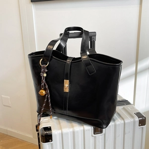 Classic black leather tote bag with gold lock and woven pendant on a metallic suitcase