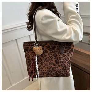 Detail of leopard print tote bag with brown bear plush charm and woven cord accessory