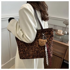 Detail view of leopard print tote bag with brown leather strap and plush bear charm