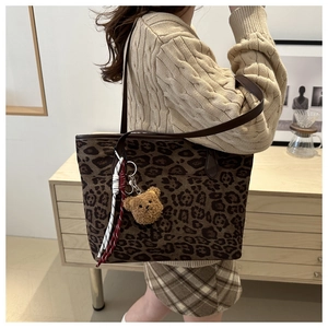Close-up of leopard print tote bag with brown plush bear charm and woven rope detail