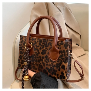 Detail view of leopard print handbag with woven bell charm and brown leather handle