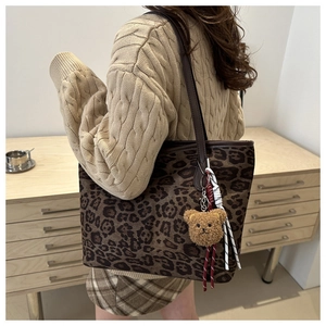 Detail of leopard print tote bag with plush bear charm and woven cord accessory
