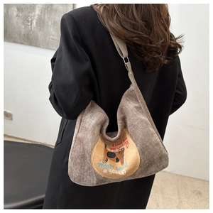 Detail van bruine corduroy hobo tas met schattige kattenborduring op de schouder van model