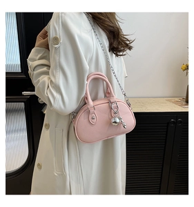Detail of pink pebbled leather handbag with silver chain and ball charm on white coat