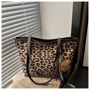 Detail of leopard print tote bag with brown leather handles and plush bear charm