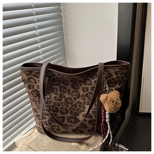 Detail view of large leopard print tote bag with brown faux leather trim and plush bear charm