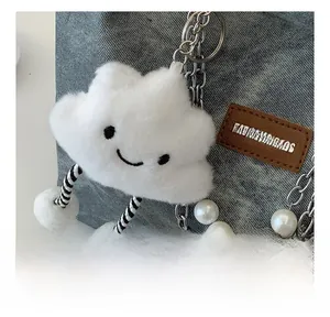 Detail of white plush cloud charm with smile face and pearls on a denim bag