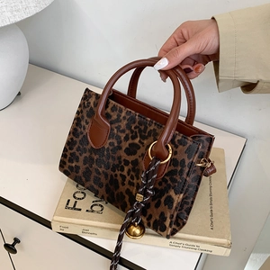Leopard print box handbag with brown leather handles and decorative bell ornament