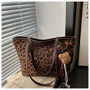Detail of leopard print tote bag with brown plush bear charm and woven handles