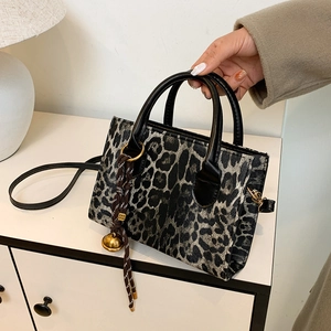 Vintage leopard print handbag with black handles and creative pendant in minimalist interior