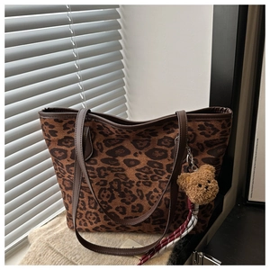 Detail of leopard print tote bag featuring a plush bear charm and leather handles