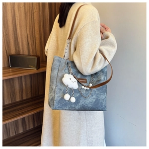 Detail of blue washed canvas tote bag with leather strap, plush cloud charm, and pearl chain