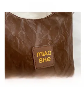Detail showing the brown wrinkled texture and logo plaque of the vintage shoulder bag