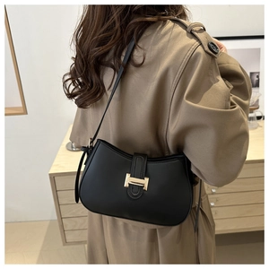 Detail of matte black leather shoulder bag with gold buckle on khaki trench coat