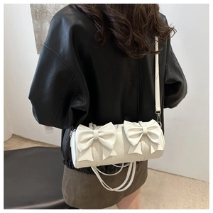 Detail der weißen Zylindertasche mit dekorativen Schleifen und Lederstruktur am Schultergurt