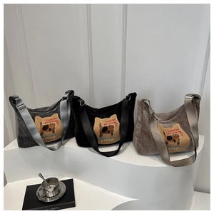 Drie corduroy hobo-tassen in grijs, zwart en bruin met kattenpatches op een wit platform