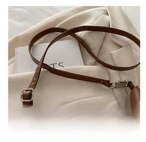 Close-up of deep brown leather shoulder strap with silver buckle on a blazer background